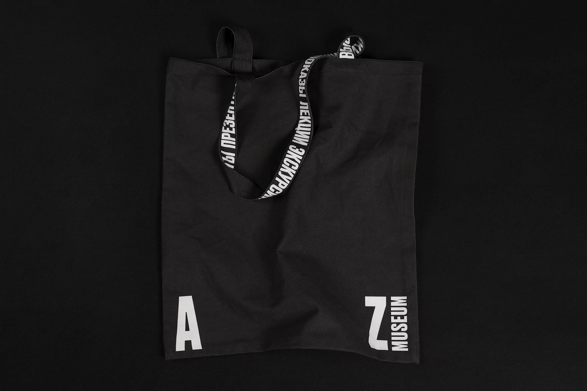Black tote bag with white 'A Z Museum' text on a black background. Reusable shopping bag with text along the straps.