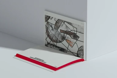Open book with abstract geometric illustrations and red spine resting against a minimal white corner wall.