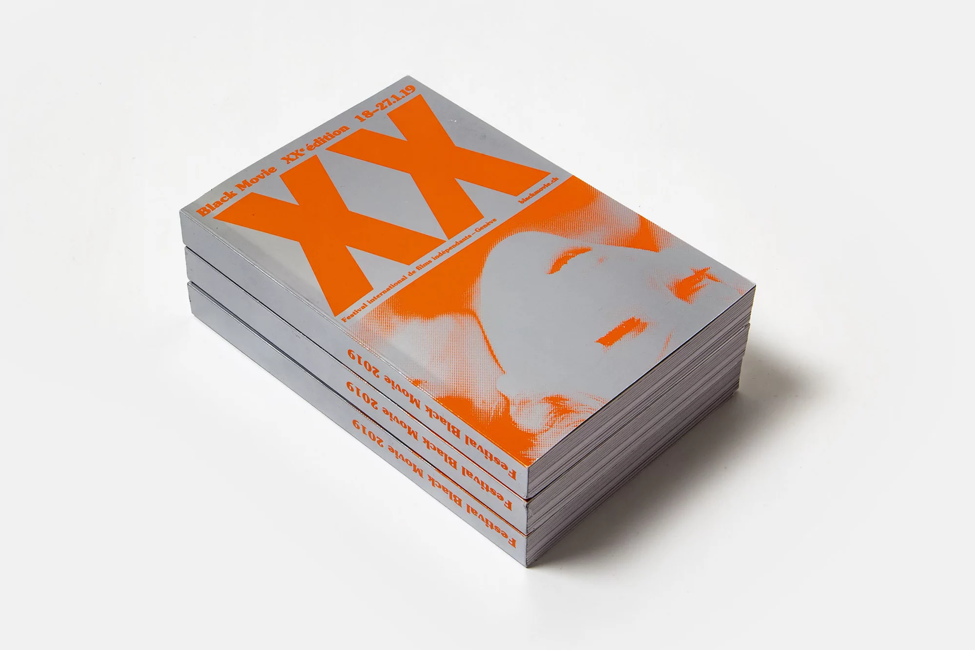 Stack of black movie festival books with orange XX and face graphic on a plain white background in a studio photograph.