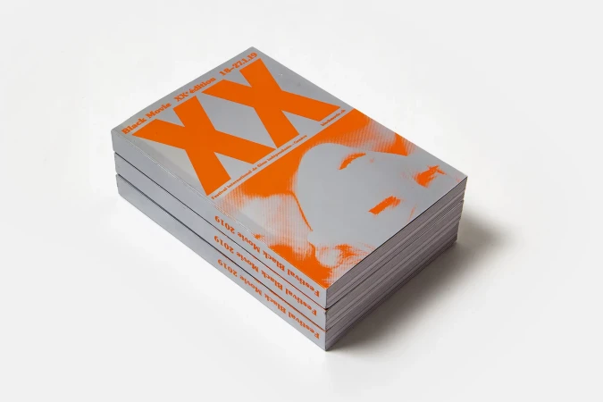 Stack of black movie festival books with orange XX and face graphic on a plain white background in a studio photograph.