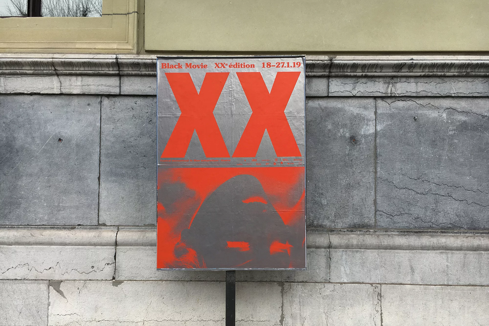 Red and silver festival poster featuring large XX typography mounted on an ornate stone building exterior wall
