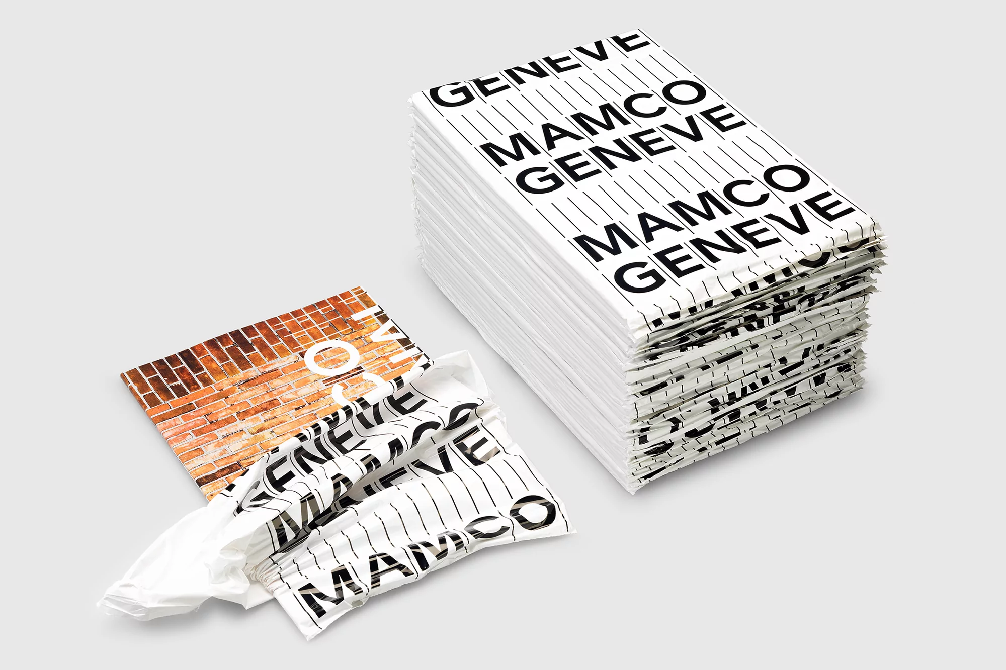 Stack of MAMCO GENEVE branded paper with crumbled branded paper and brick image on table against a light gray background.