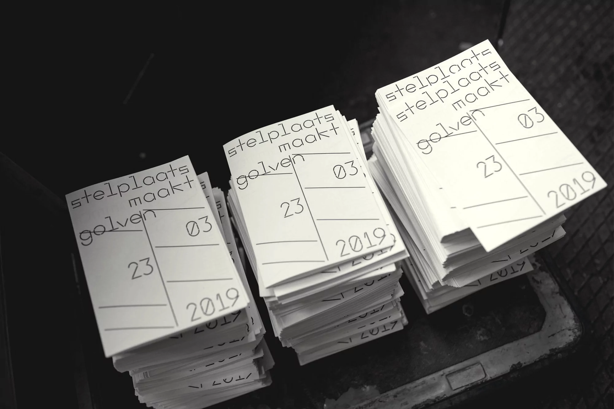 Stacks of white pamphlets with black typography, featuring publication details and graphic design elements, neutral tones and high angle.