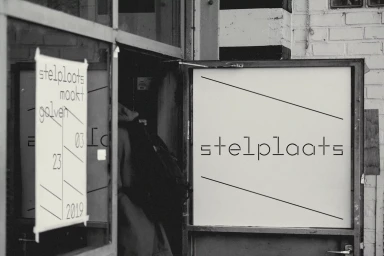 Black and white image of Stelplaats brand identity featuring typography on a sign and poster on a doorway.