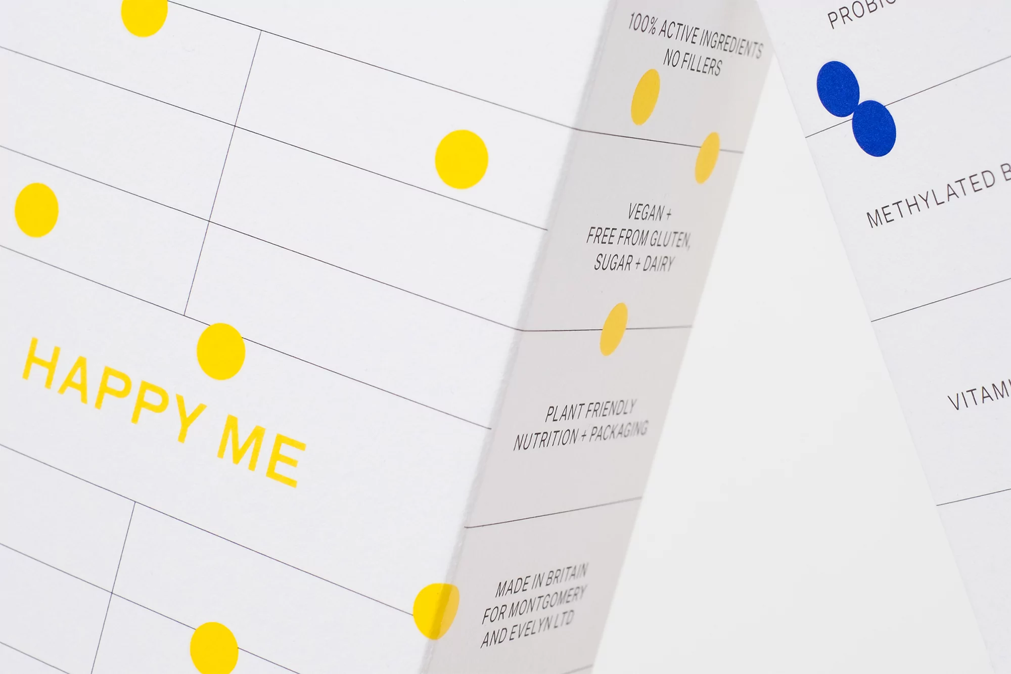 Minimalist product packaging featuring the text 'Happy Me' and health benefit claims, using a clean, grid-based design with yellow and blue accents.