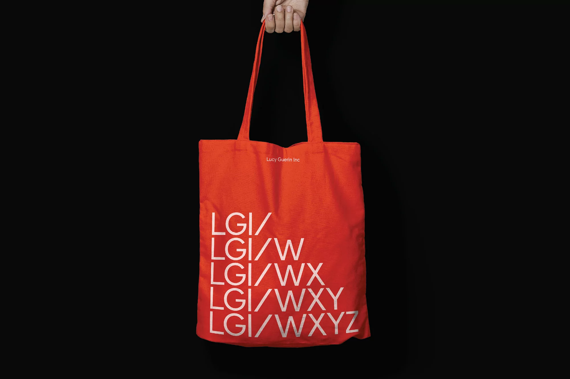 An orange tote bag with white text, held by a hand against a black background, perfect for marketing or product showcase.