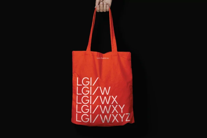 Hand holding a bright red tote bag with white typography against a solid black background