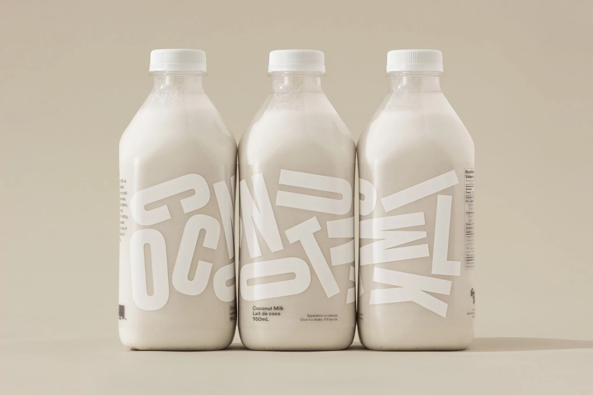 Three clear bottles of coconut milk with white caps stand in a row against a neutral background, labels prominently display brand text.