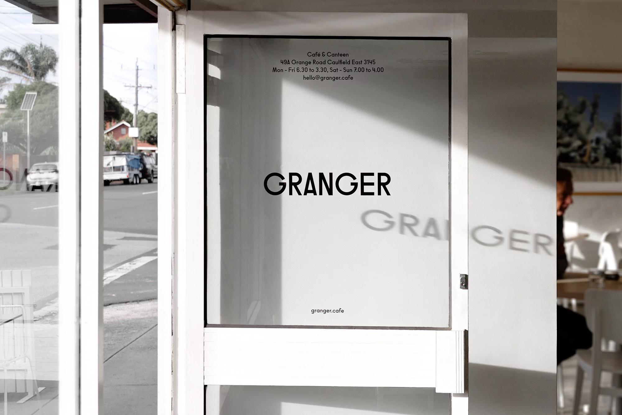Exterior view of Granger cafe featuring a glass door with cafe name and information, showcasing the entrance and surrounding street view.