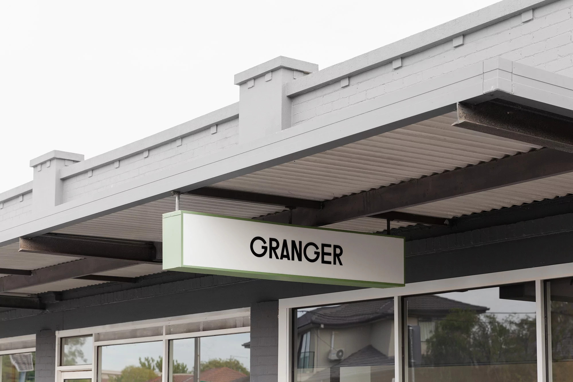 Exterior view of a building with a rectangular sign reading 'Granger' attached to its grey roof. Large windows visible below.
