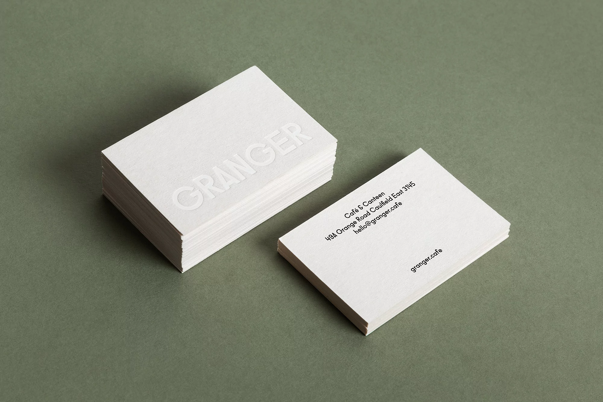 Stack of white business cards with embossed lettering on a green background, providing a minimalist and professional presentation.