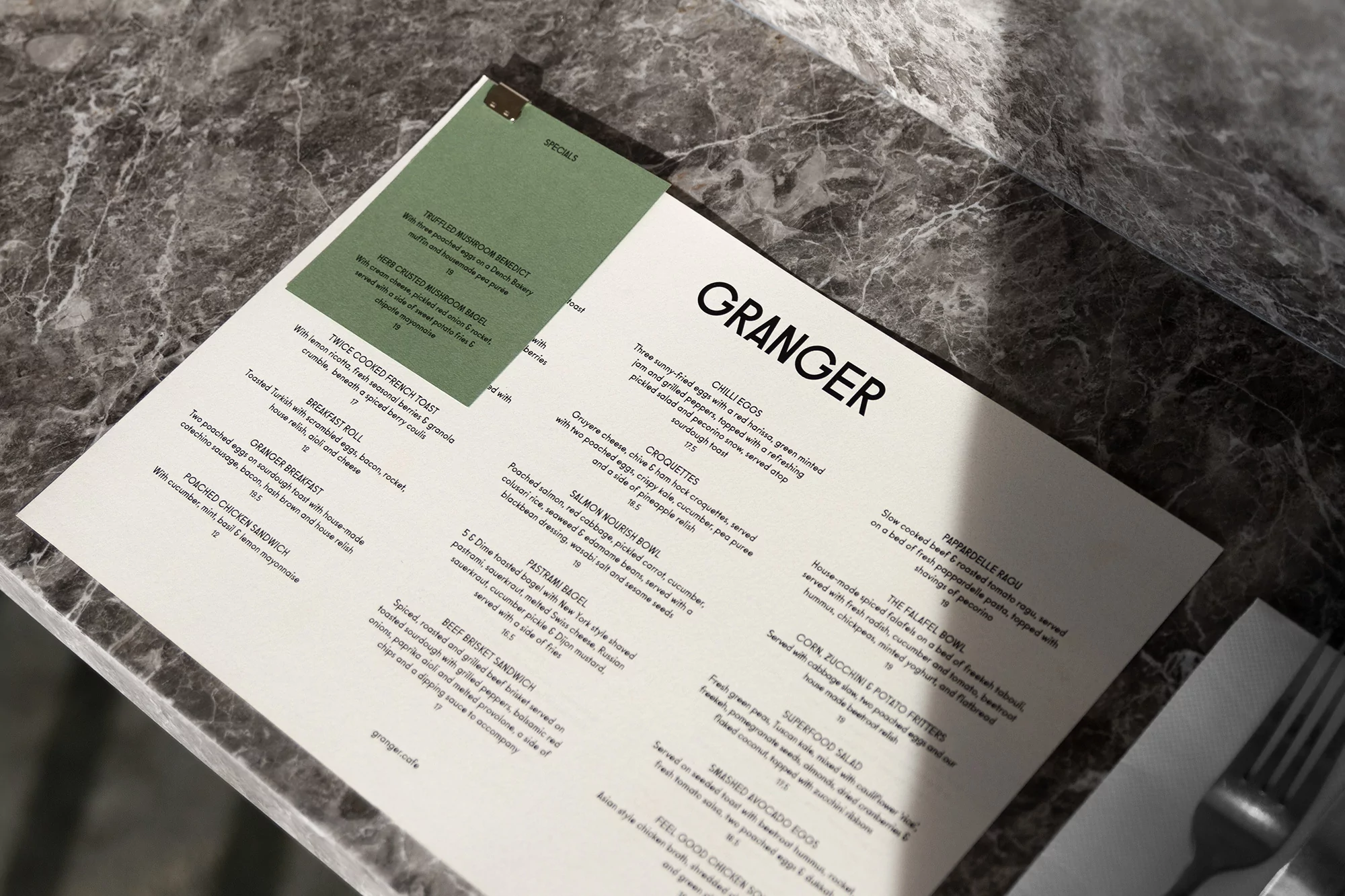 Granger restaurant menu displayed on a marble table, featuring food items like chilli eggs, croquettes, and the falafel bowl.