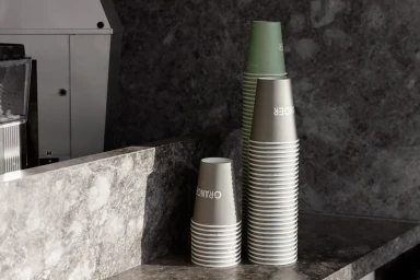 Stacked paper coffee cups featuring Granger branding resting on a dark marble countertop in a cafe setting.