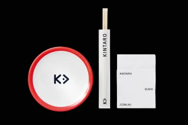 Kintaro brand identity layout featuring a round white plate with a red rim, chopsticks in a branded sleeve, and a napkin.