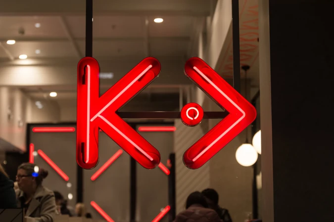 Bright red neon logo sign hanging in an interior setting with blurred figures in the background