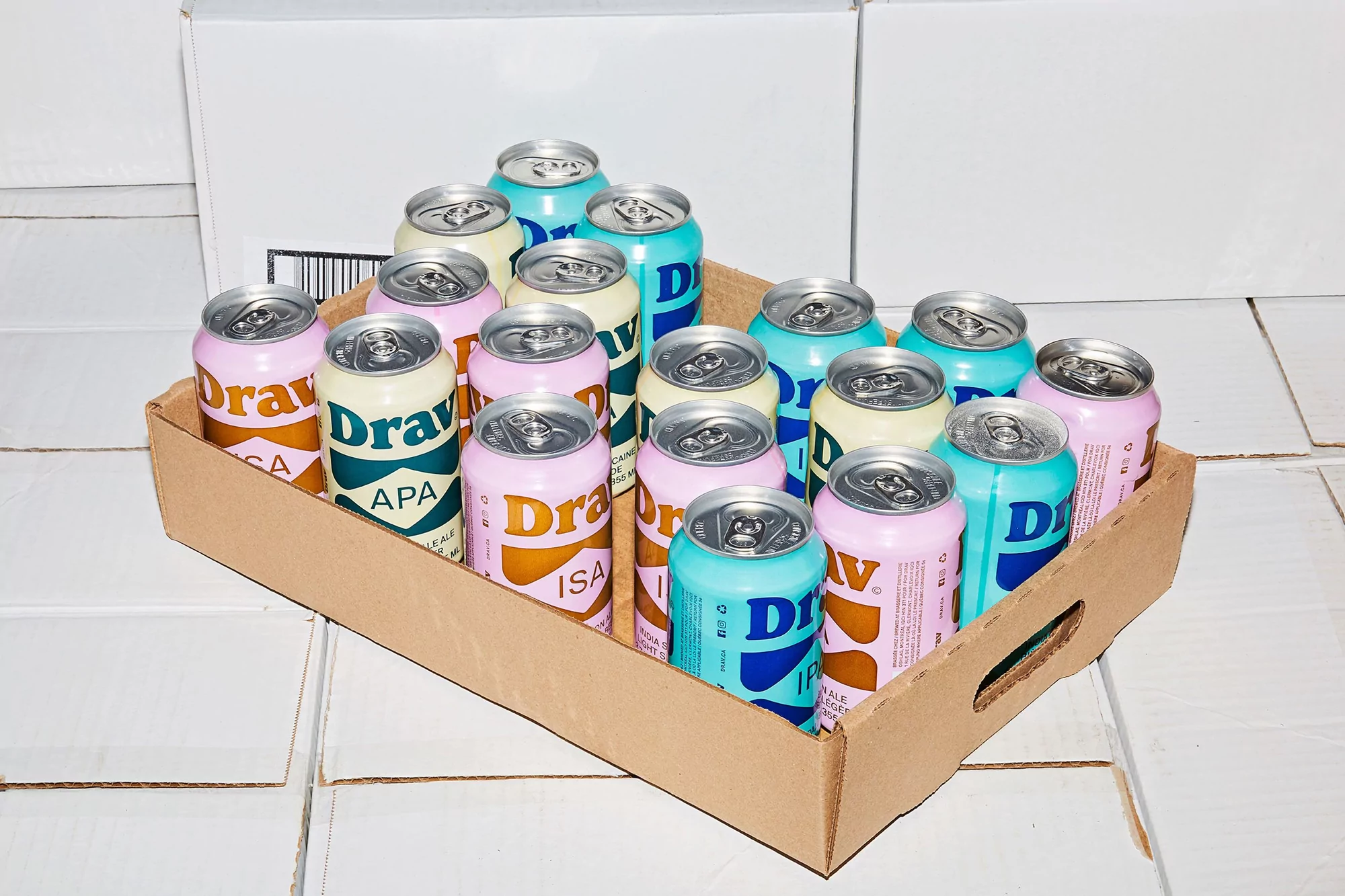 Assorted variety of colorful Drawl IPA and ISA cans in a cardboard tray on white tiled floor in a bright indoor setting.