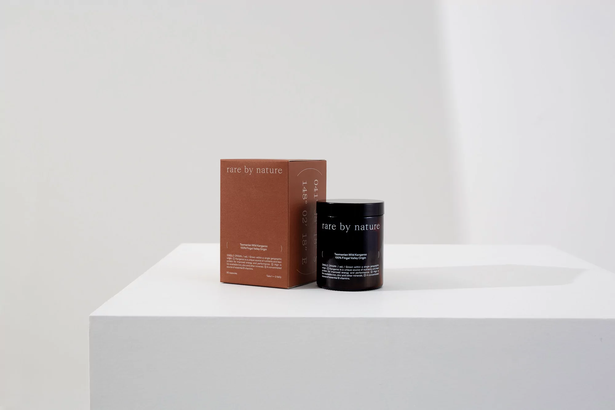 Product shot of brown cosmetic jar and product box for Rare by Nature on a white platform against a neutral background.
