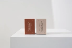 Two rectangular product packaging boxes standing on a white pedestal against a plain white studio background.