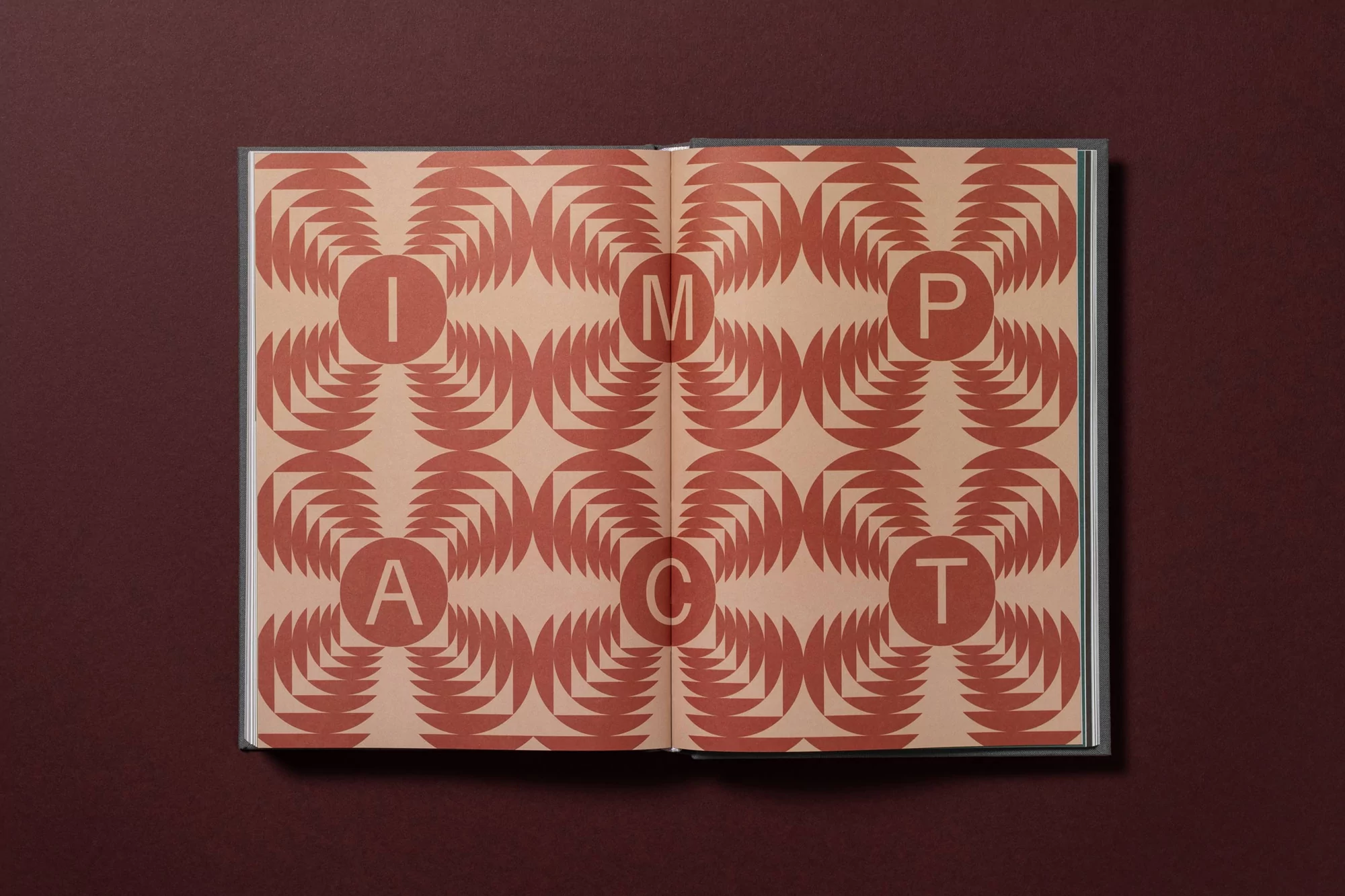 Open book with graphic pattern and the word IMPACT across two pages, on a red background. Book design with geometric shapes and letters.