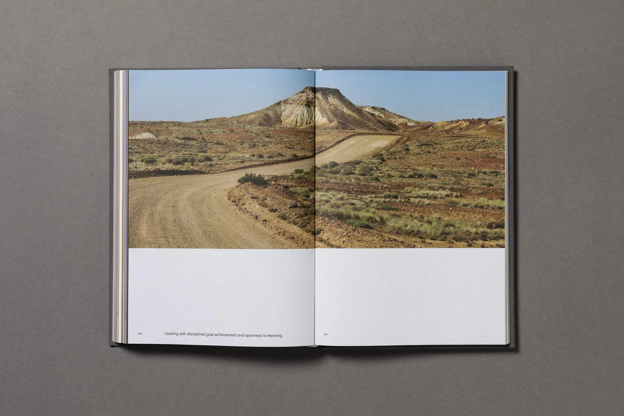 Open book displaying a photograph of a winding dirt road leading to a mesa under a blue sky, showcasing arid landscape photography.