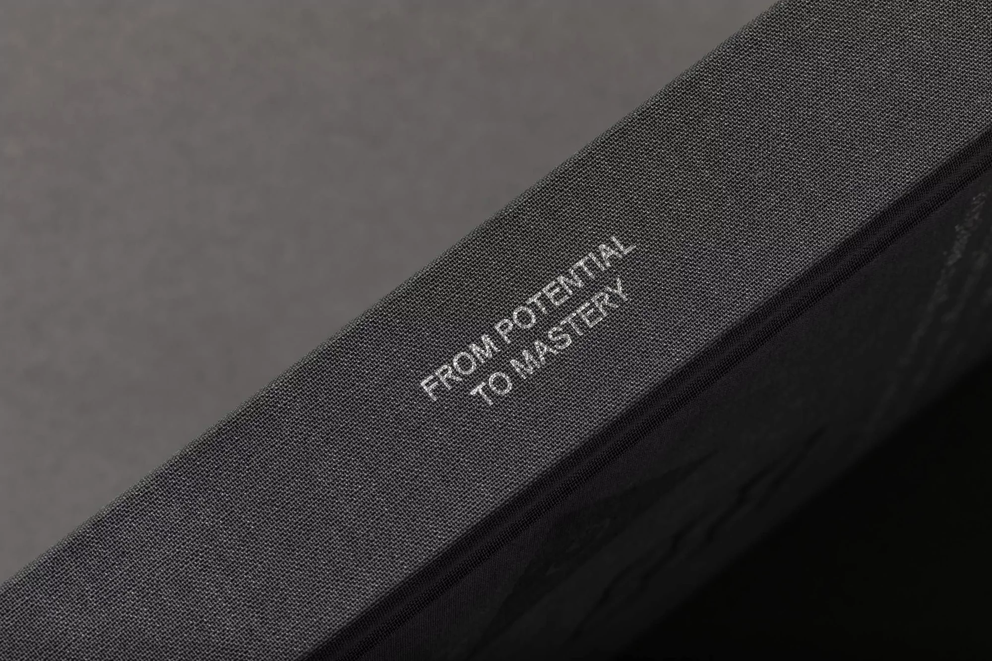 Close-up of a gray, textured book with the inscription 'FROM POTENTIAL TO MASTERY' visible on its cover.