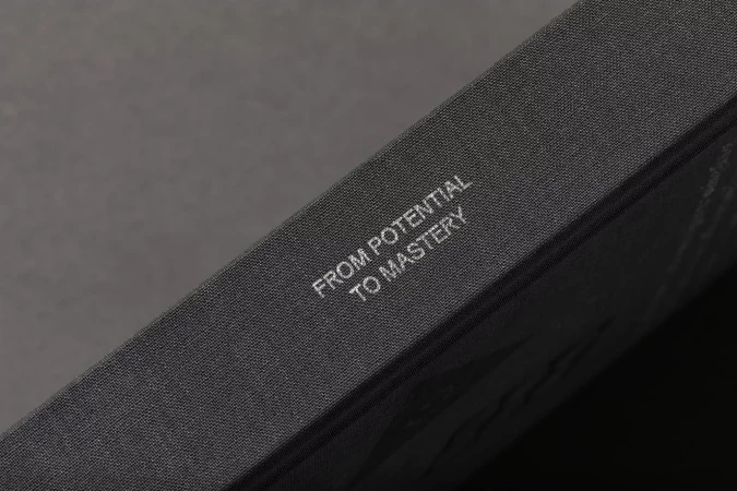 Close-up of a gray, textured book with the inscription 'FROM POTENTIAL TO MASTERY' visible on its cover.