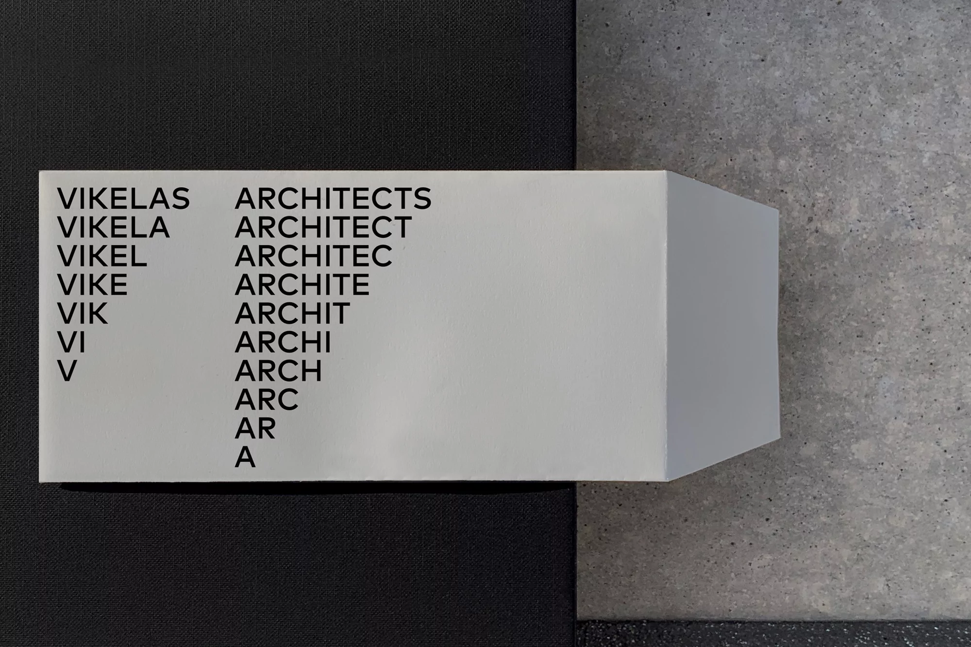 Geometric architectural block showcasing the name 'Vikelas Architects' in a diminishing typography, set against textures of gray and black.