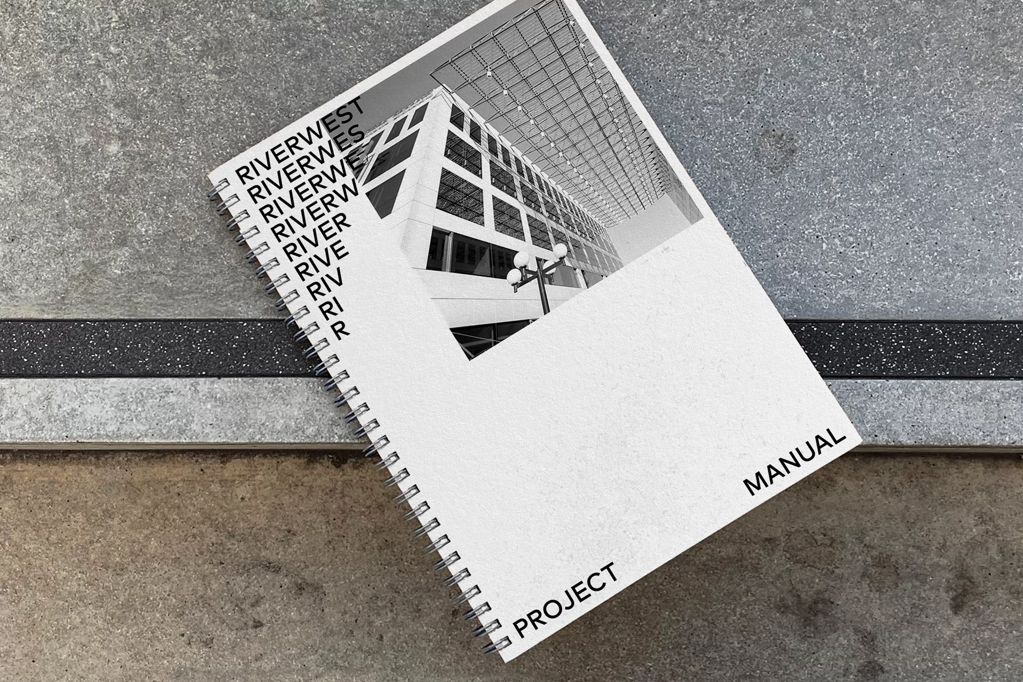Elevated view of spiral-bound project manual featuring an architectural image, set on a textured concrete surface with a dark inlay.