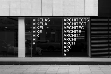 Monochrome storefront window featuring white typographic branding for Vikelas Architects with receding letter columns