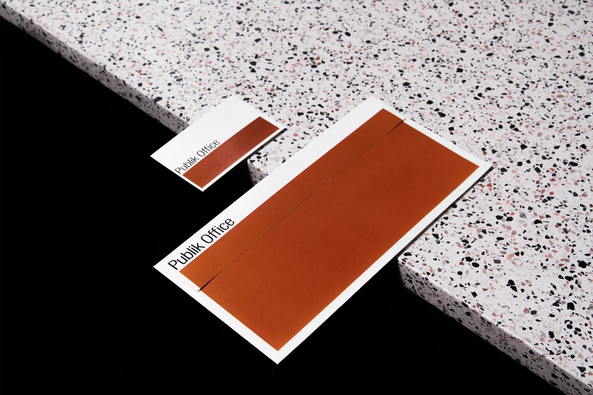 Two rectangular cards, one large and one small, rest on a speckled surface against a black background, both featuring an orange stripe.