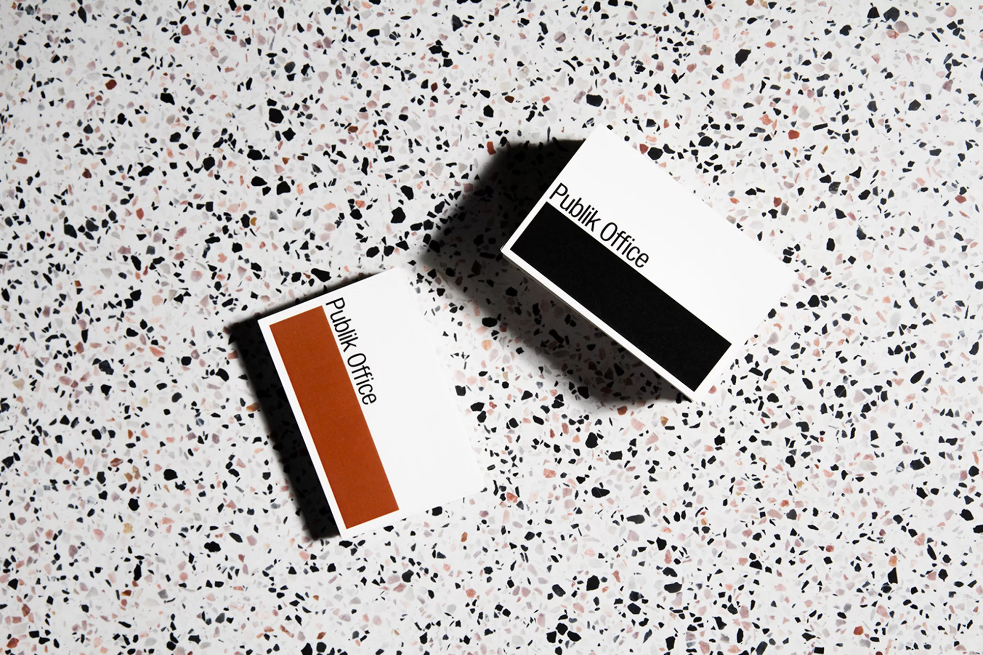 Two business cards for Publik Office with a modern design, set on a speckled surface, showcasing minimalist branding and visual clarity.