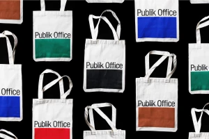 Top-down view of canvas tote bags with Publik Office branding and colorful block prints arranged on a black background
