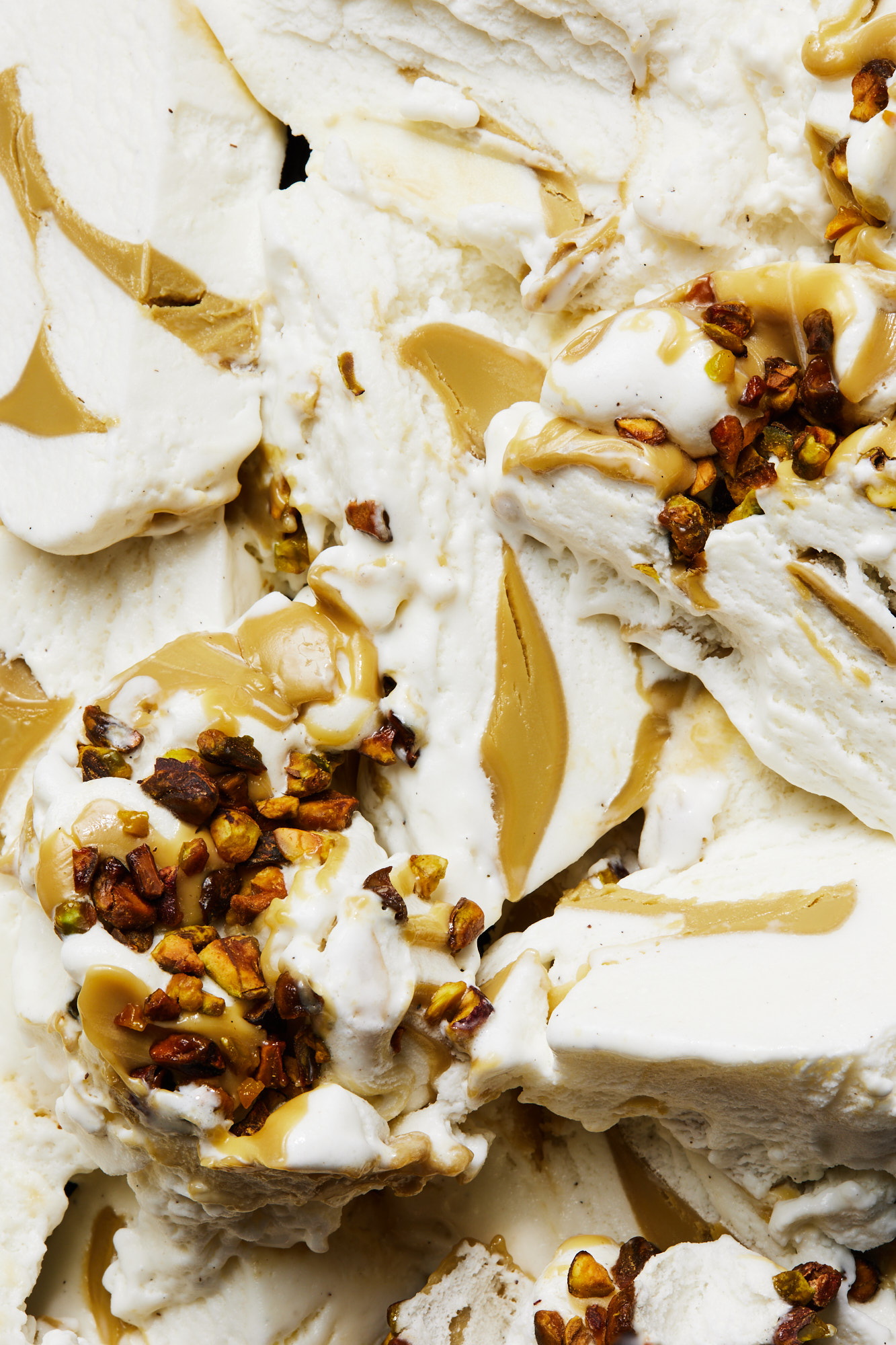 Close-up of white ice cream featuring caramel drizzle and nut pieces, highlighting textures and dessert components.