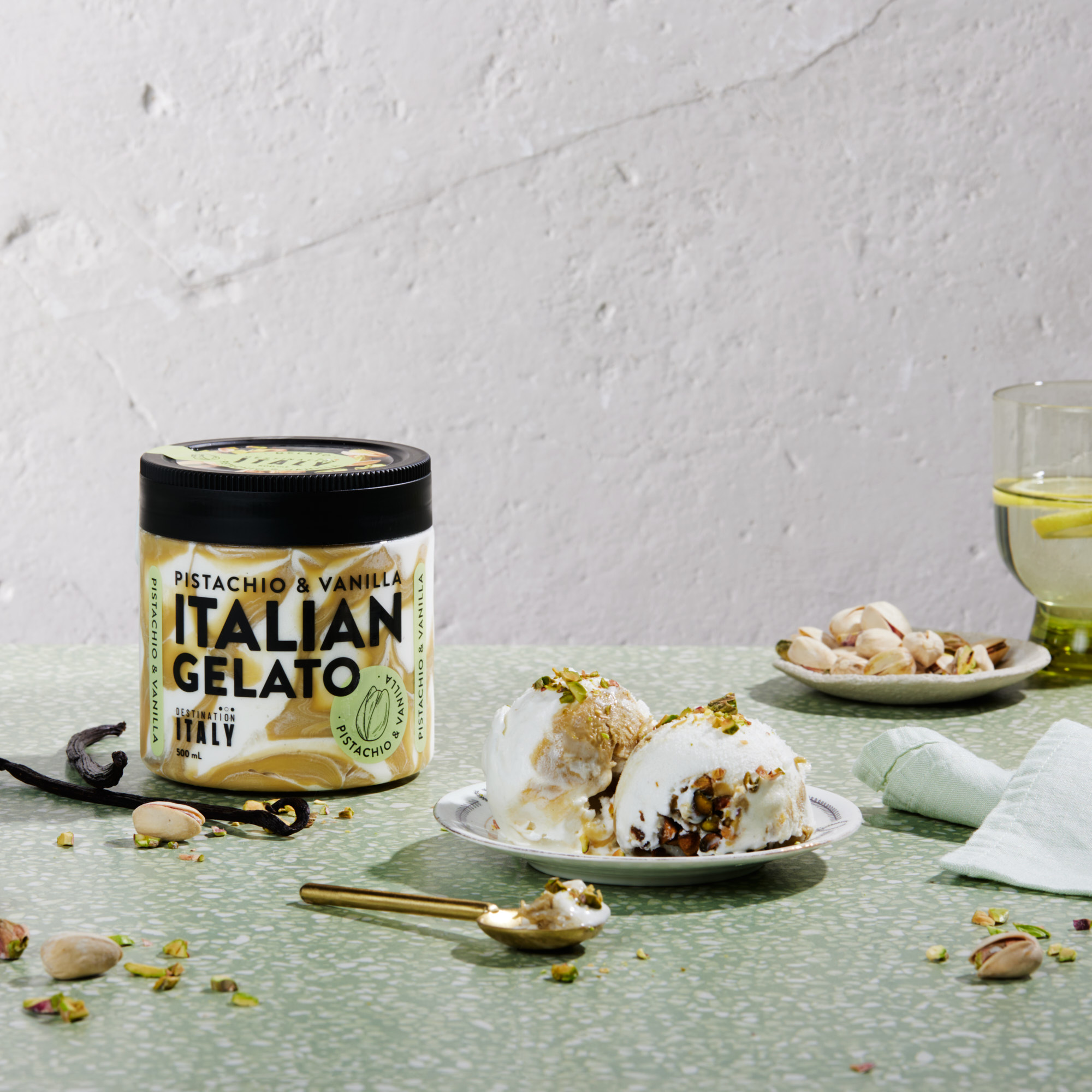 Italian pistachio and vanilla gelato in a jar, served on a plate with pistachios, and a glass of water with lemon on a green table.