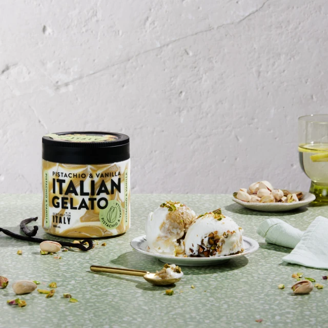 Italian pistachio and vanilla gelato in a jar, served on a plate with pistachios, and a glass of water with lemon on a green table.