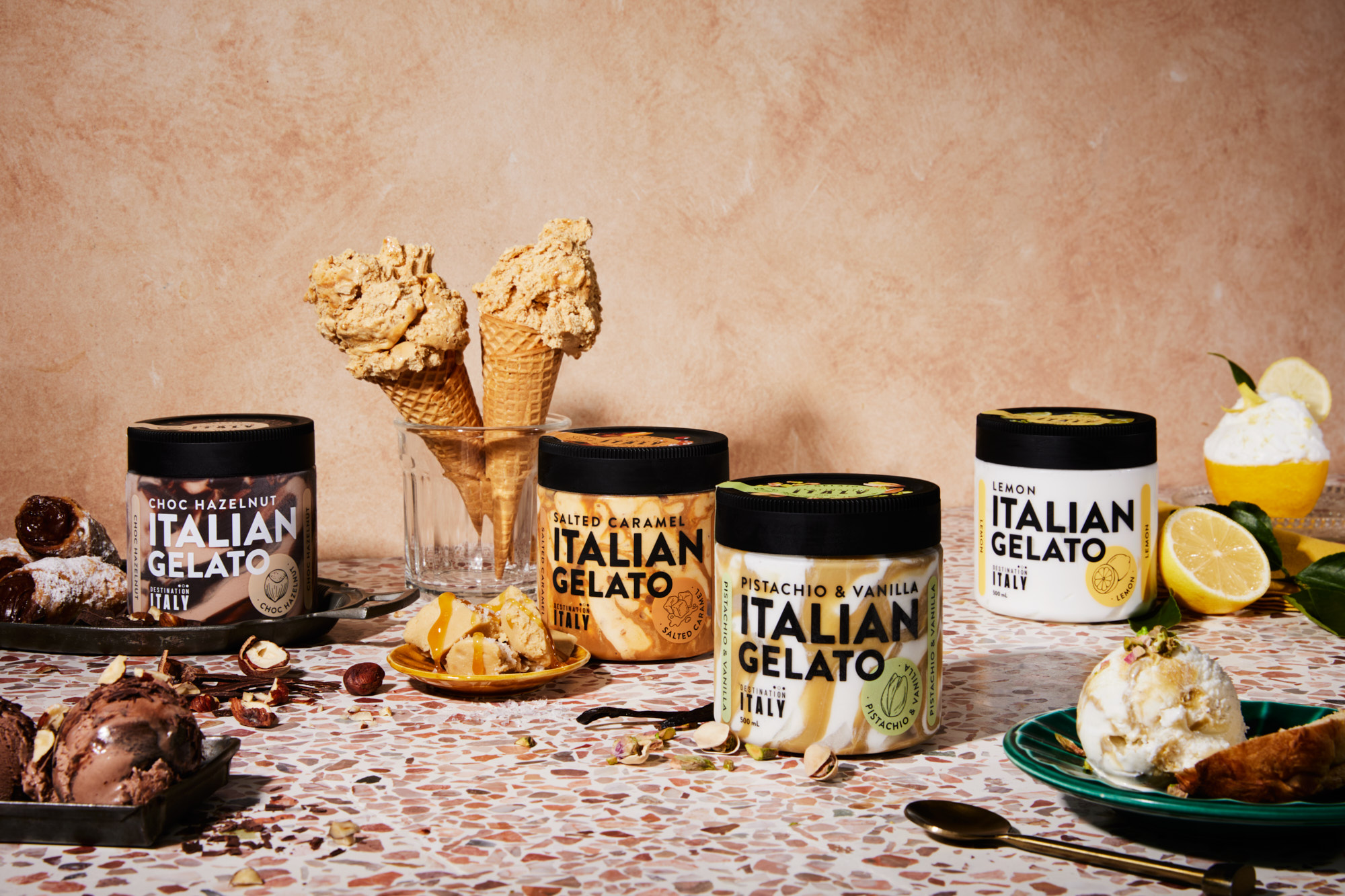 Assortment of Italian gelato in jars and cones with flavors like chocolate hazelnut, salted caramel, pistachio & vanilla, and lemon.