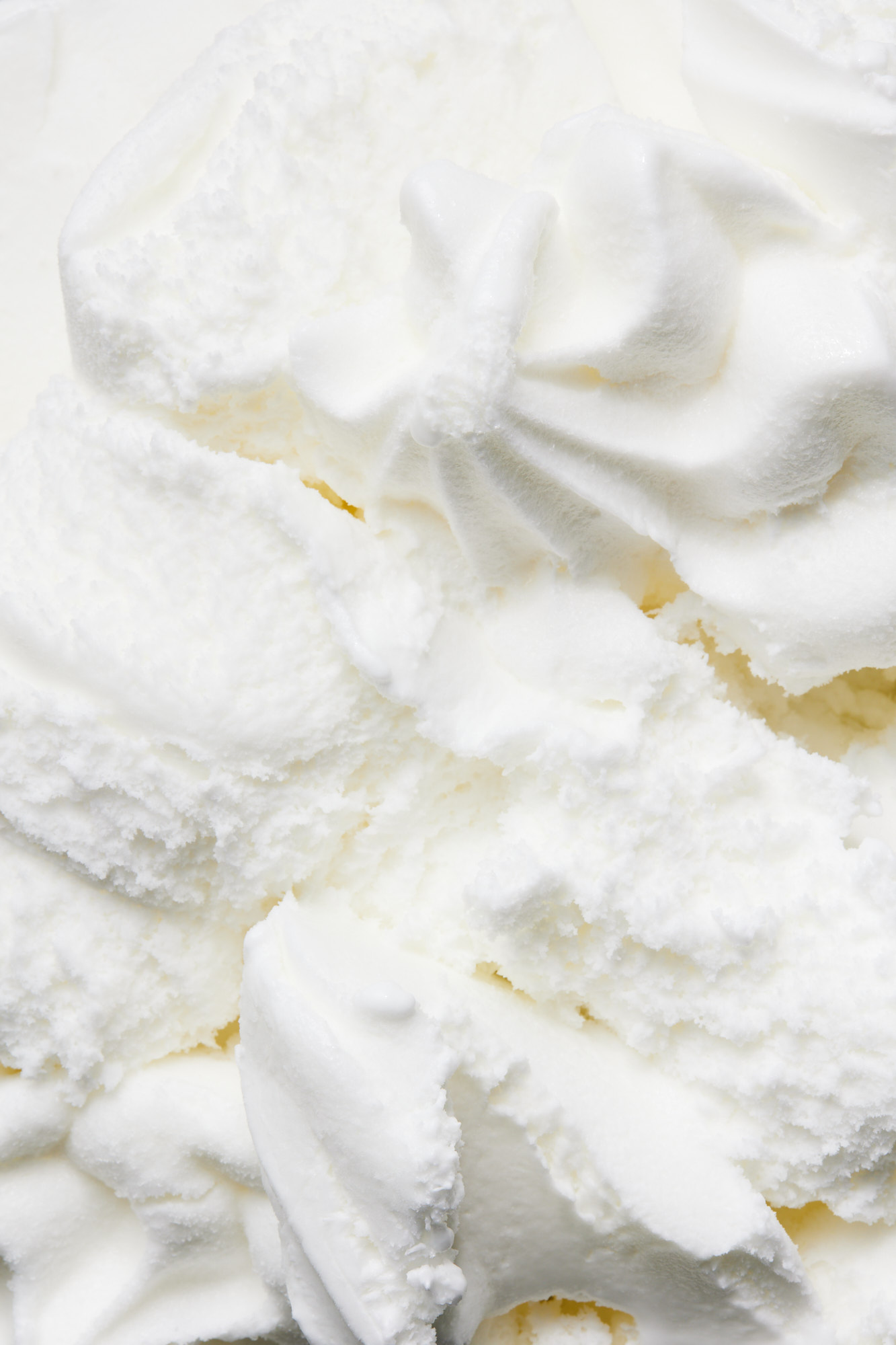 Close-up of a creamy white dessert topping, possibly frosting or whipped cream, featuring soft peaks and swirls. Food photography.
