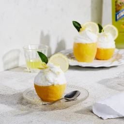 Lemon sorbet served inside hollowed lemon halves topped with whipped cream on glass plates with a spoon.