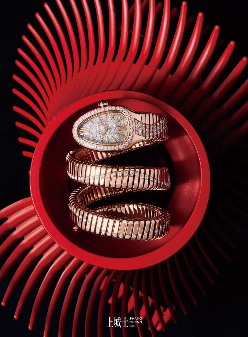 Rose gold wristwatch coiled in red bowl on black background with spiral-like red decor, jewelry fashion, luxury watch.