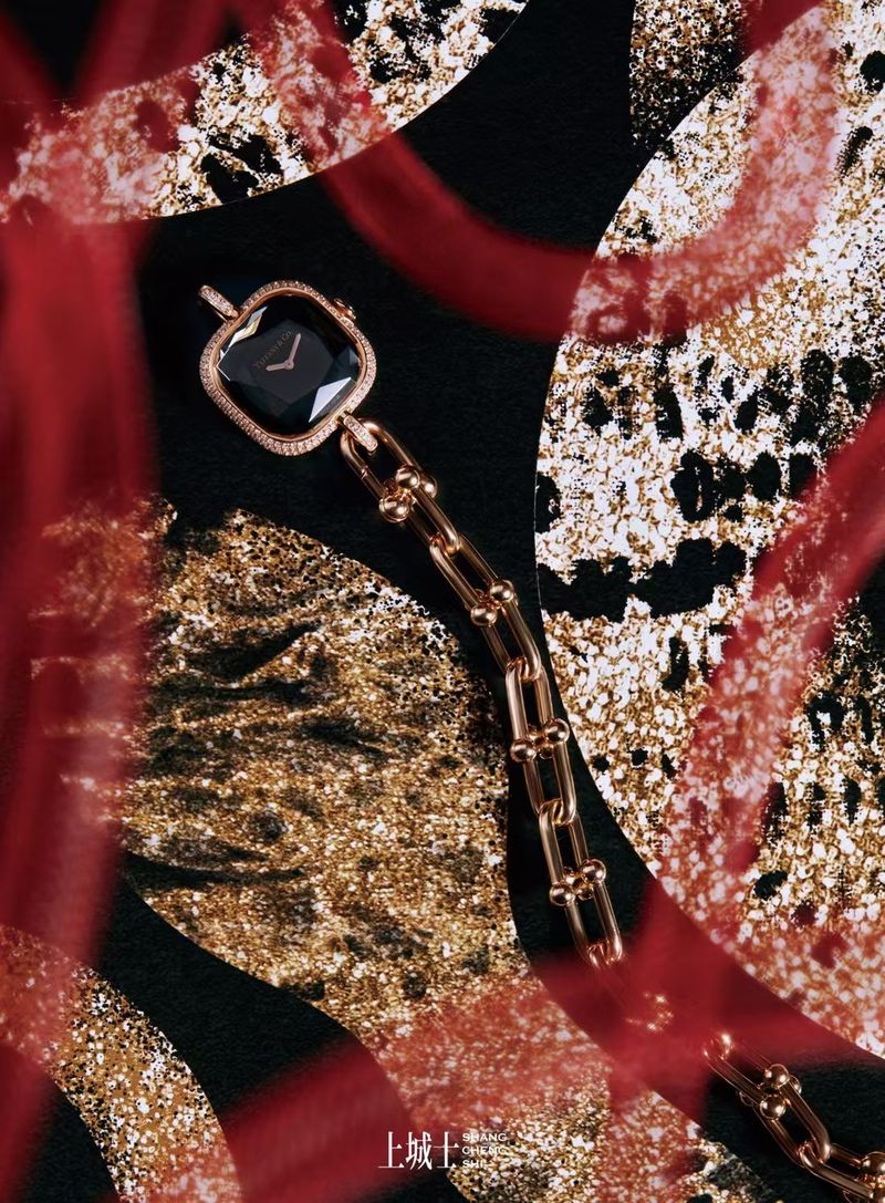 High-angle shot of a gold necklace-watch hybrid against a black, white, gold, and red abstract patterned surface.