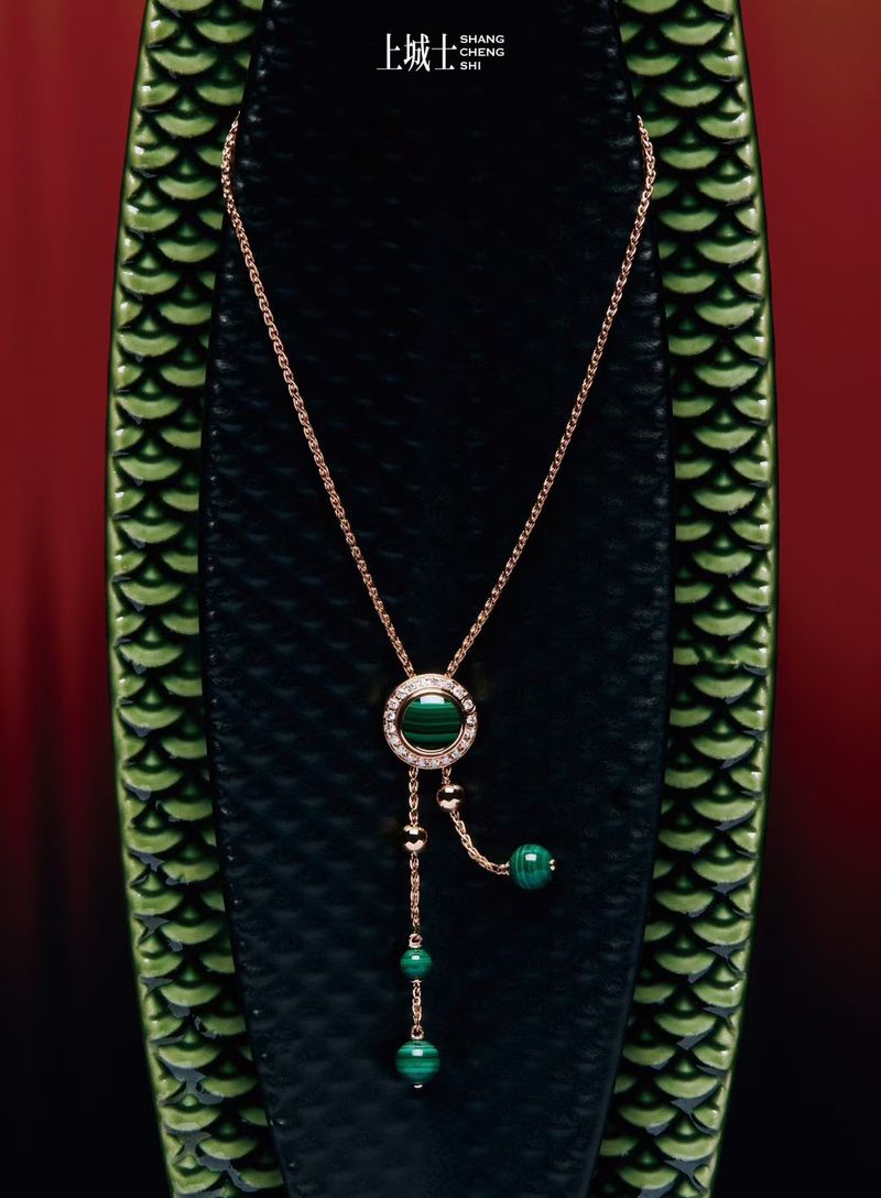 Elegant gold necklace with green gemstones displayed against textured dark and green backdrop. Jewellery still life studio shot.