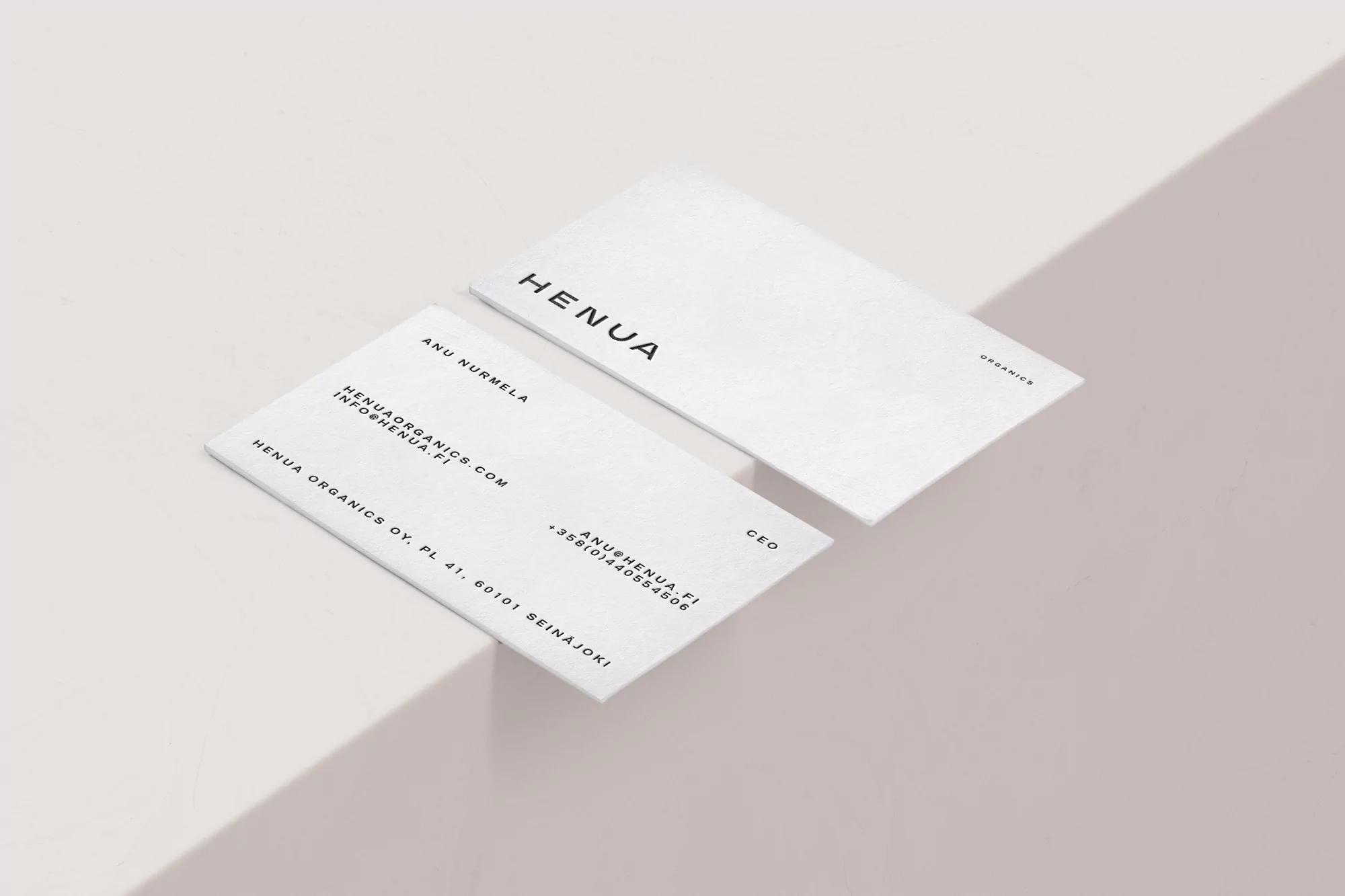 Two minimalist Henua Organics business cards are displayed against a soft beige backdrop, each card showcasing the company's brand and contact details.