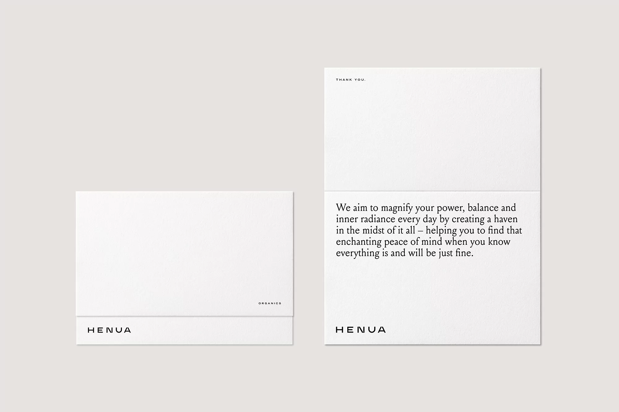 Two white Henua cards are displayed on a light grey surface, one with text and the other folded with just the Henua logo showing.