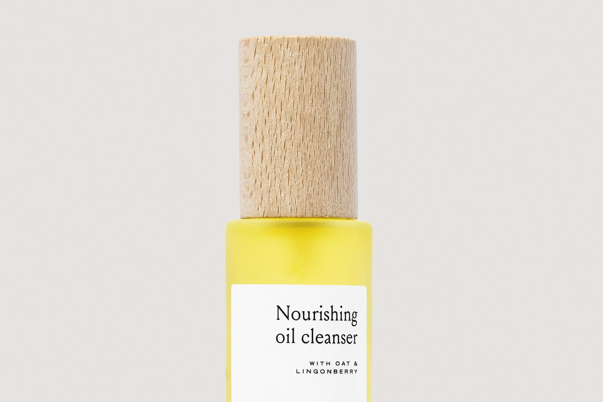 Bottle of yellow oil cleanser with wooden cap, featuring a minimalist white label on a neutral background, product photography.