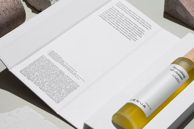 Nourishing oil cleanser product bottle resting inside an open white packaging box with printed text on light grey background