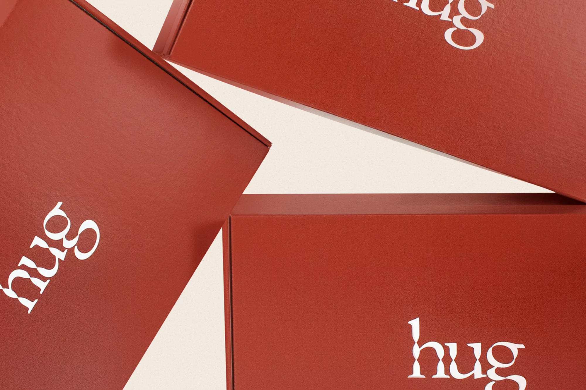 Close-up of stacked terracotta-colored boxes with the word 'hug' in white, set against an off-white background. Minimalist product photography.
