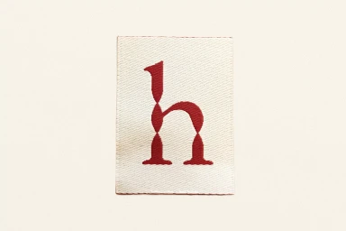 Woven fabric clothing label featuring a stylized red letter h on an off-white background