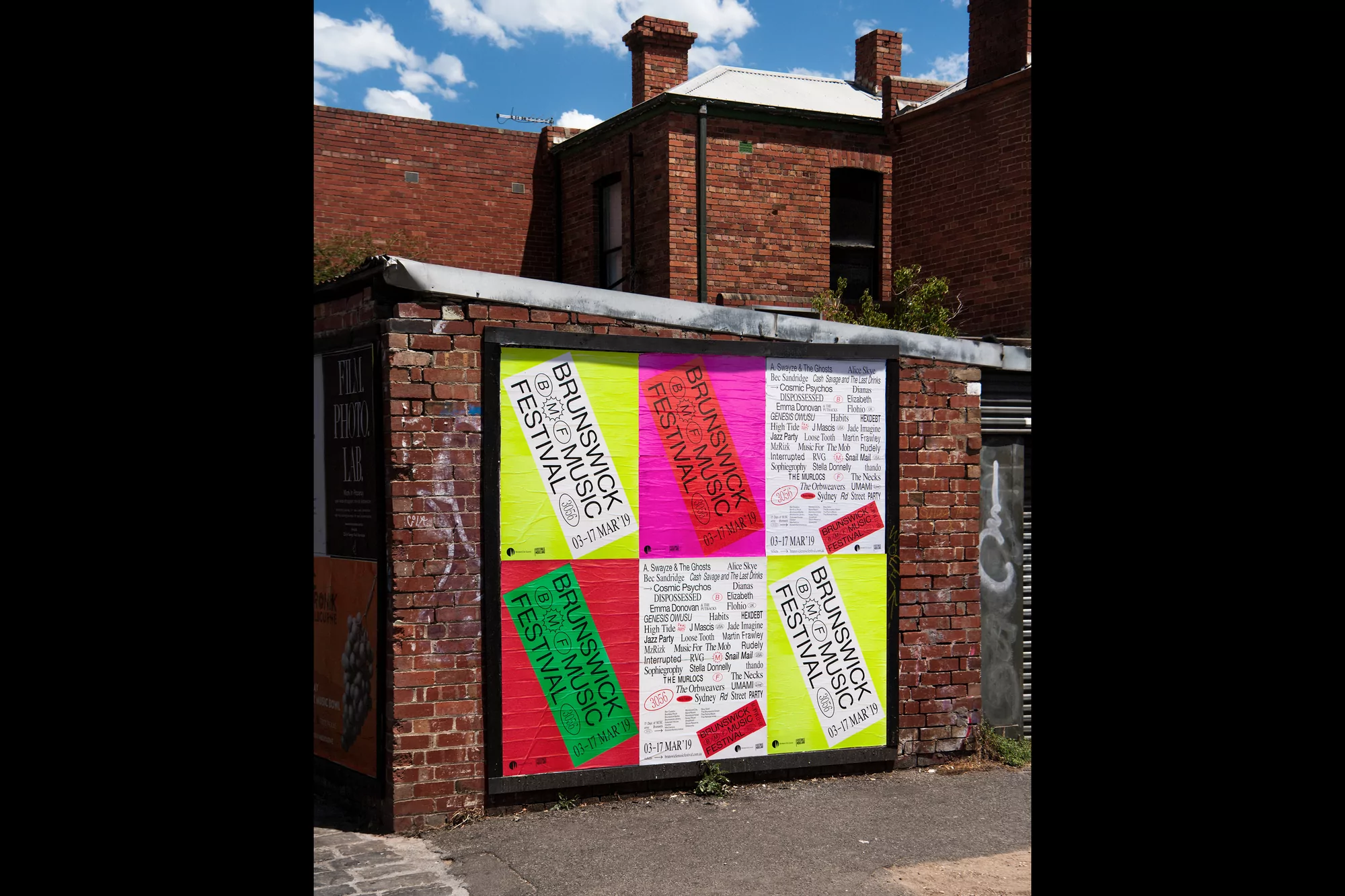 Outdoor posters promoting the Brunswick Music Festival are attached to a weathered brick wall, with building in the background.
