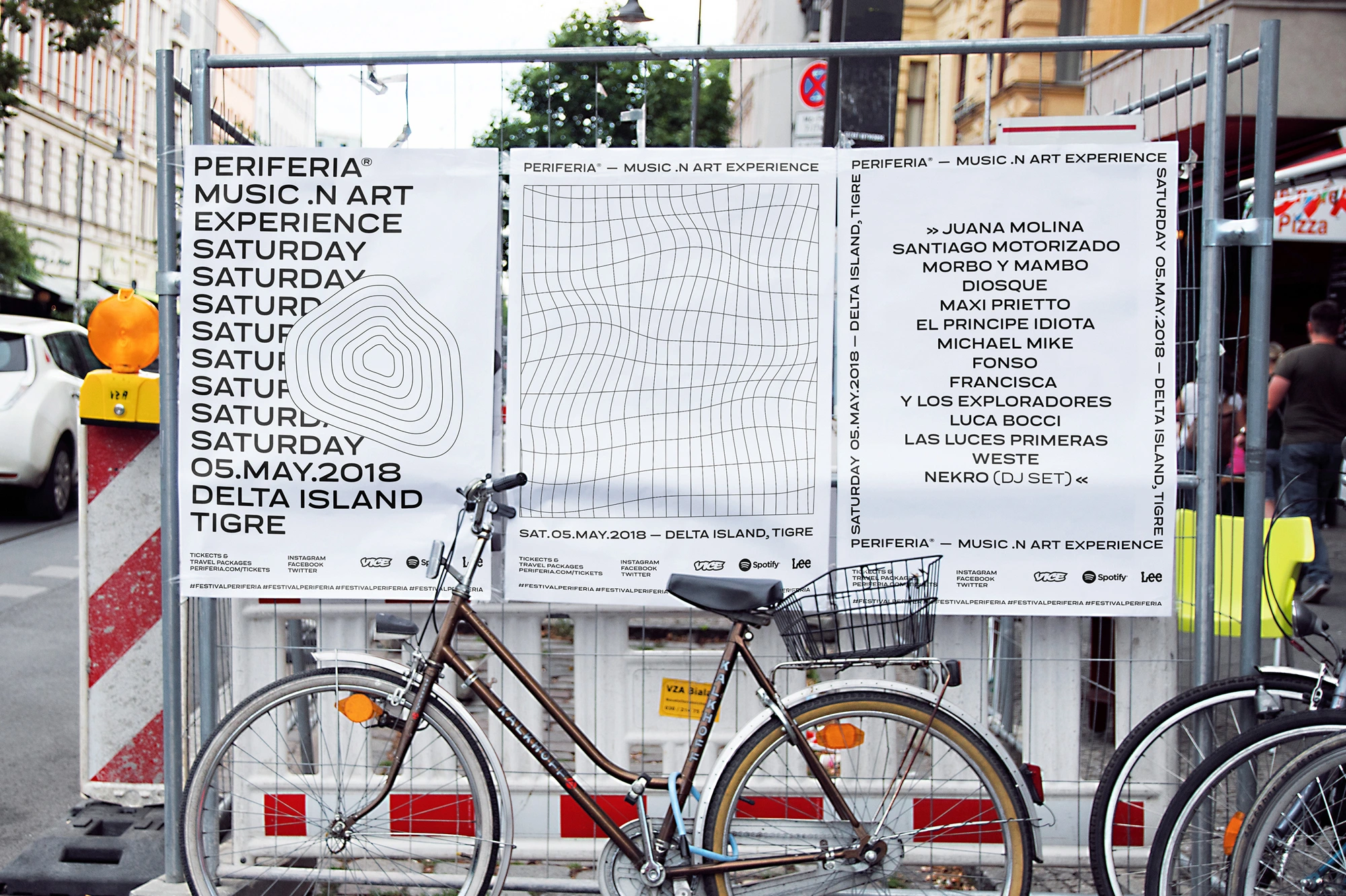 Brown bicycle parked in front of construction fencing displaying three white festival posters with typography