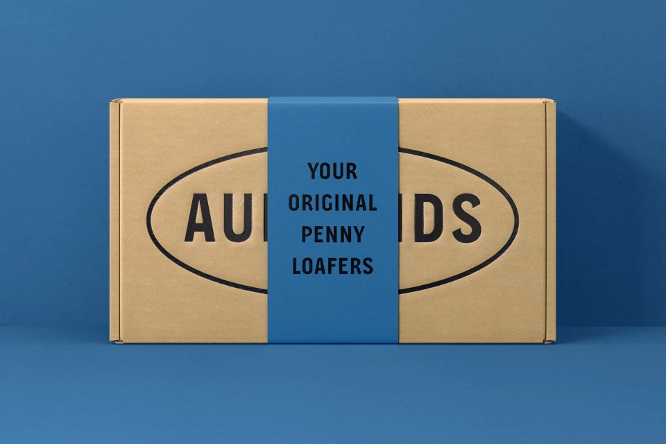 Eye-level studio shot of a cardboard box with dark text wrapped with blue paper displaying product-related information and branding.